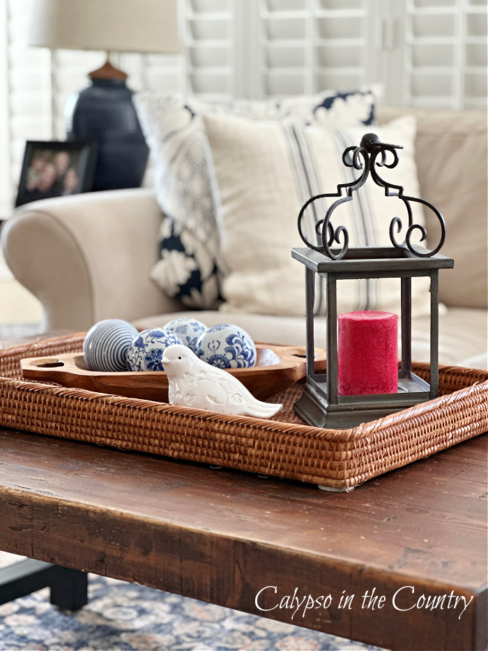 wooden coffee table decorated with rattan tray, red candle, white ceramic bird and blue porcelain spheres - middle of july ideas
