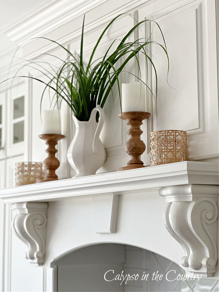 White cabinets with shelf holding wooden candlesticks and white vase with tall grasses - savoring summer