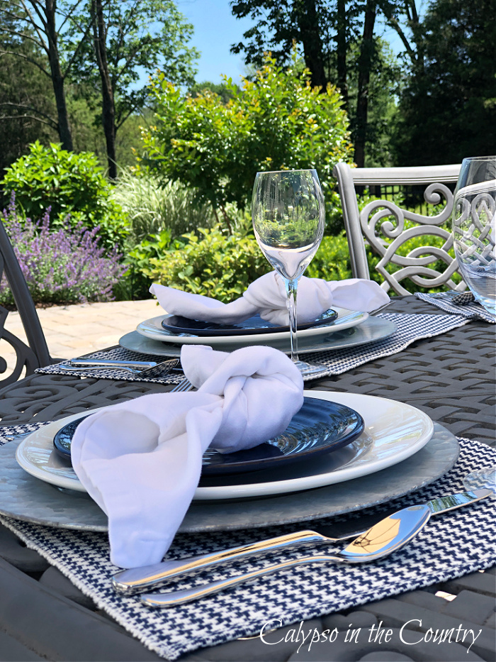 outdoor patio table set with blue and white plates and white tied napkins - savoring summer