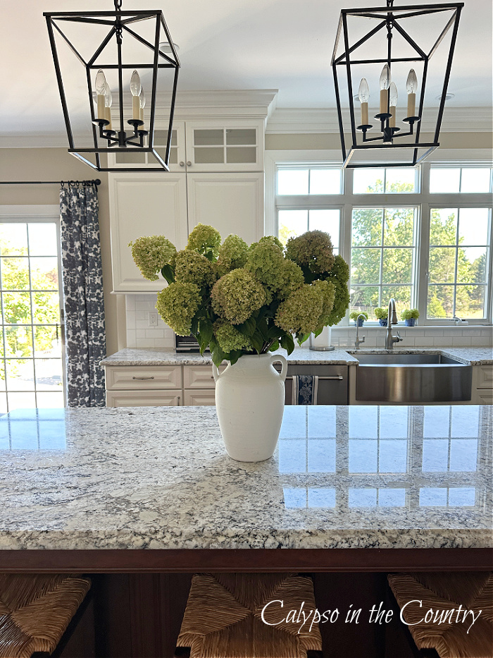 White vase filled with hydrangeas on kitchen island with two lantern lights above - decorating with hydrangeas 