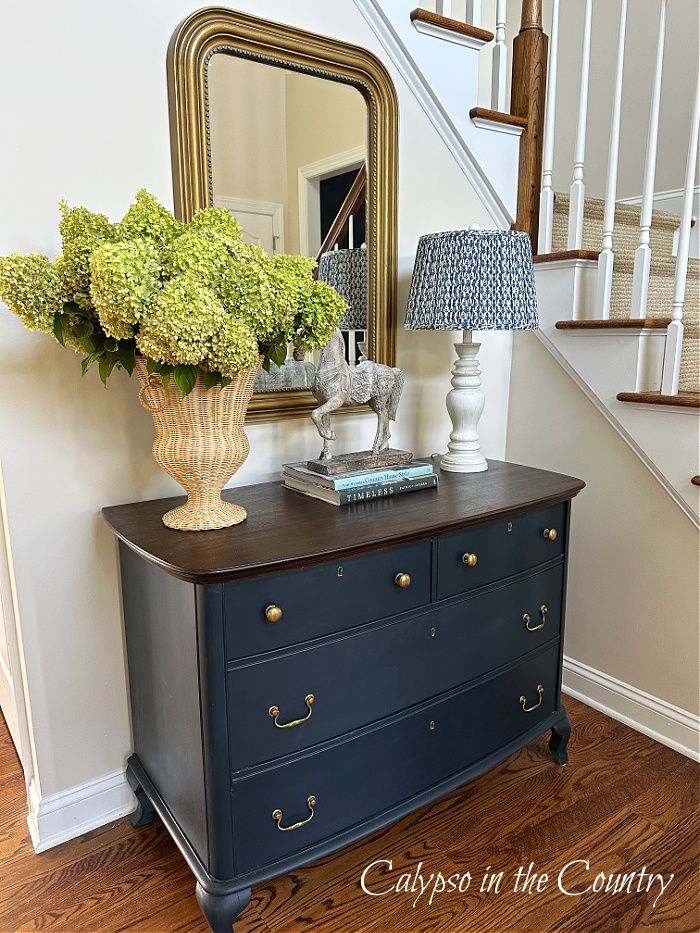 Green hydrangeas in wicker vase on blue foyer table in front of gold mirror - August recap
