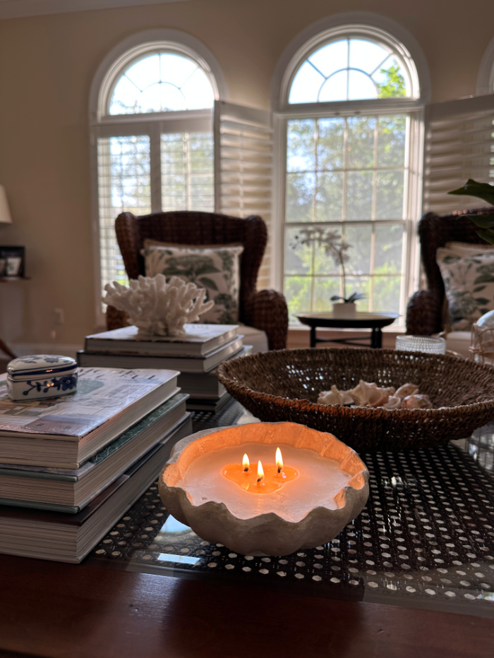 Shell candle burning on coffee table decorated with books and shells