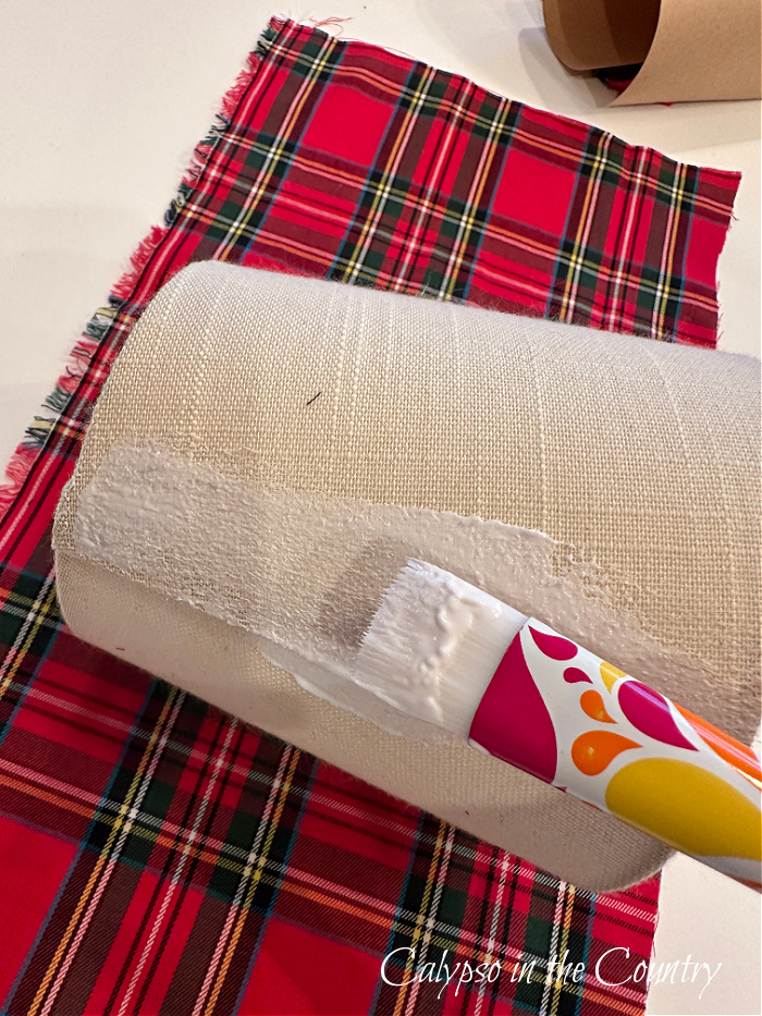 Craft brush applying Mod Podge glue to neutral chandelier shade on top of plaid fabric - DIY Plaid Lampshades