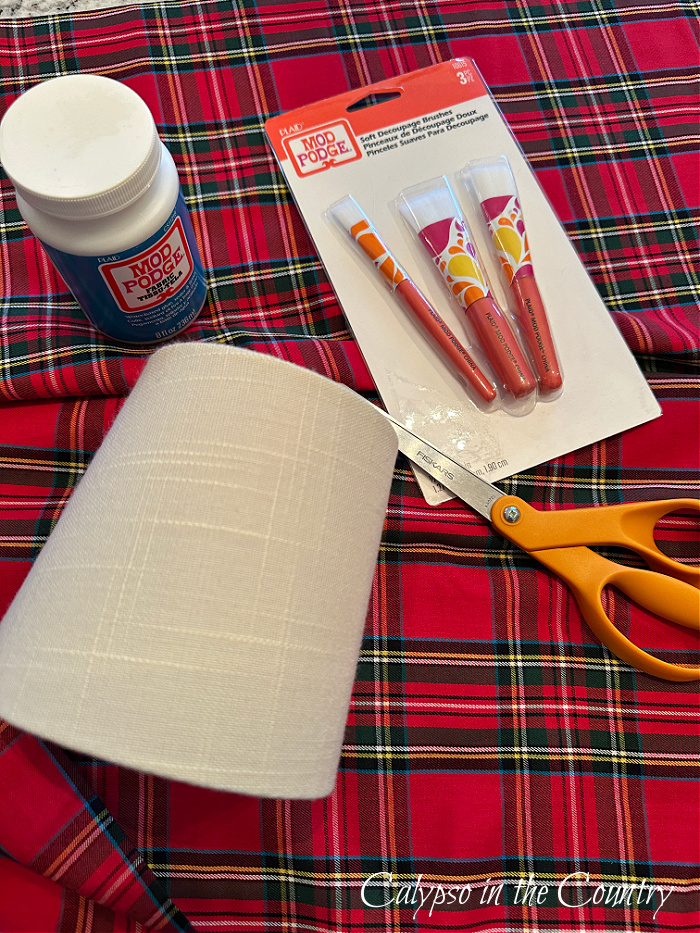 Red plaid fabric, craft brushes, scissors, small lampshade and Mod Podge container