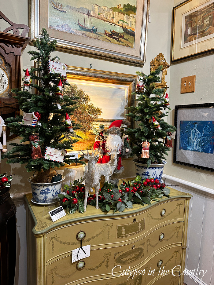 Small Christmas trees in blue and white pots on top of antique chest of drawers