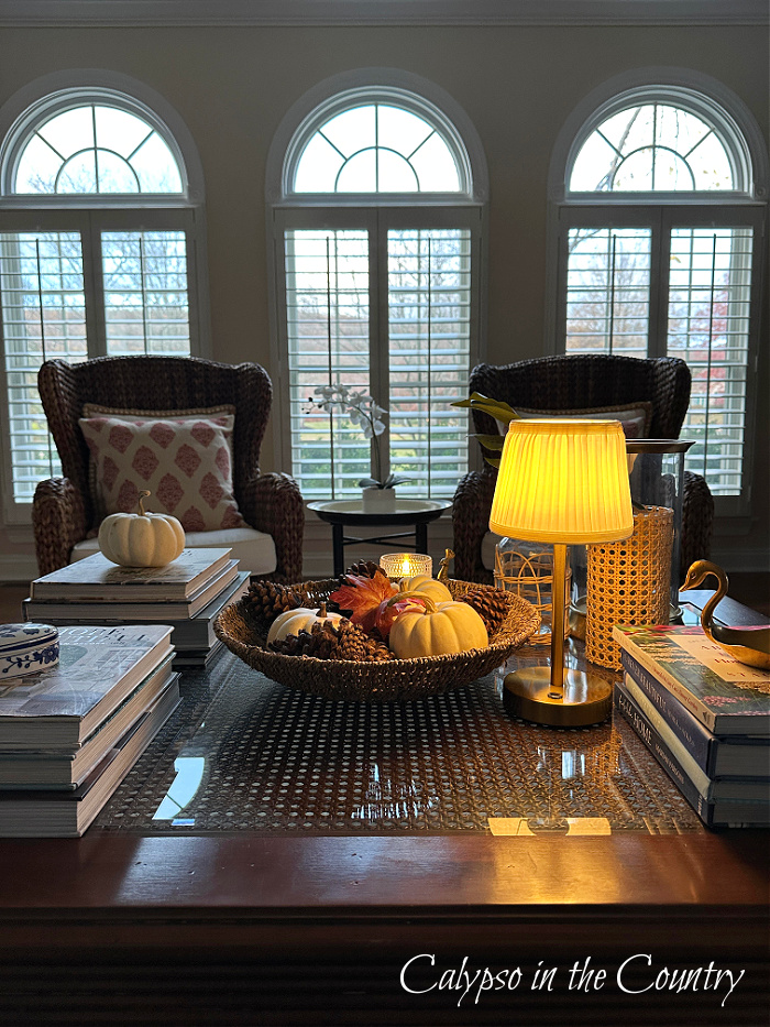 Coffee table decorated for late fall with woven bowl of mini pumpkins, stacks of books and cordless lamp - November recap