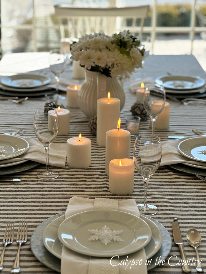 Long view of dining table with gray and white striped tablecloth, white dishes, flowers and white candles down center - winter white table setting 