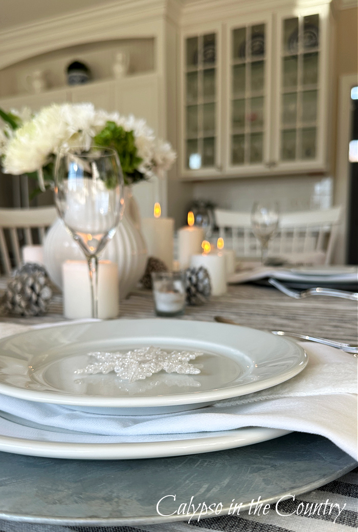 White plates and napkin close up with flowers, candles and cabinets in background