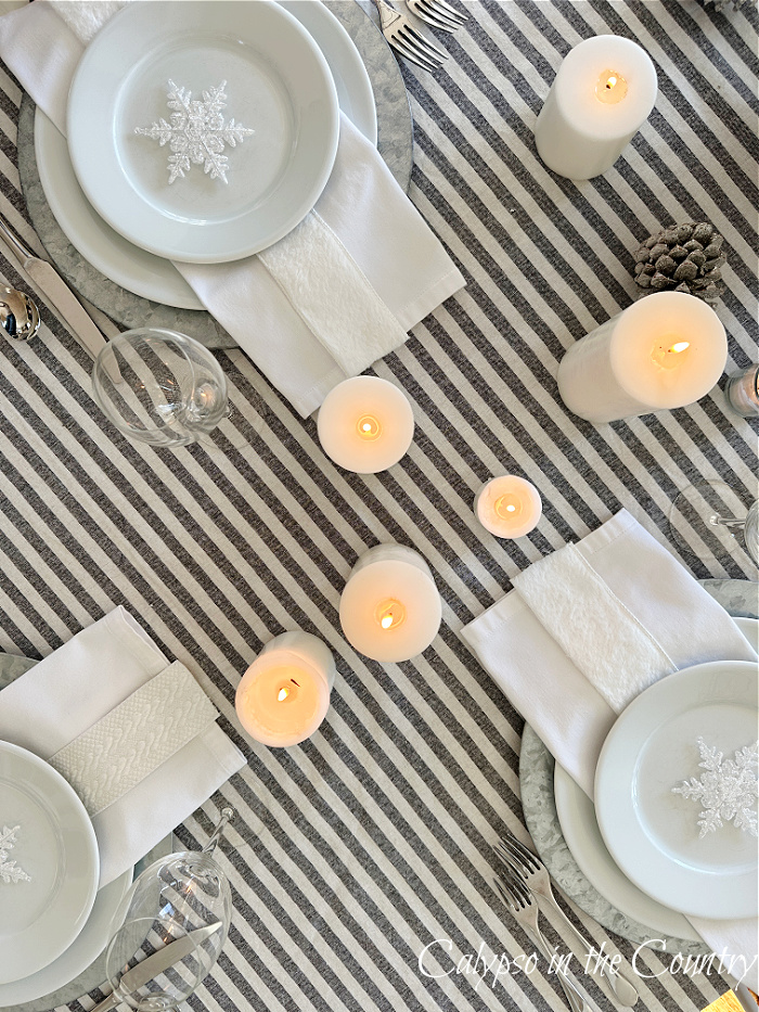 Top view of winter white table setting with three place settings, candles and striped tablecloth