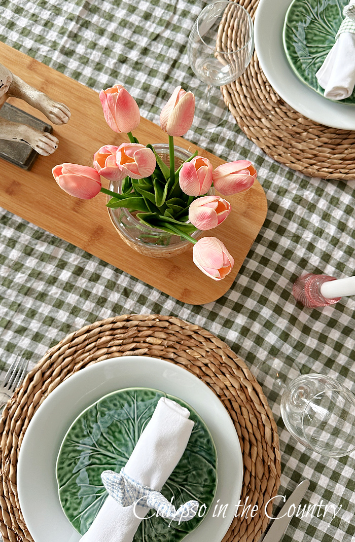 Top view of Easter brunch table setting with green gingham tablecloth and pink tulips