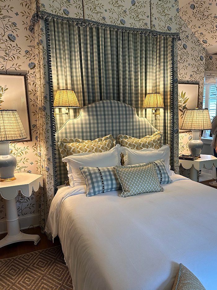 white bed with checked headboard, layered patterned pillows between two lamps with floral wallpaper behind - late march decorating ideas