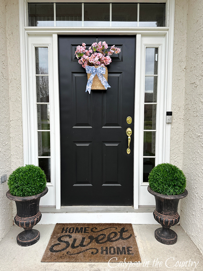 black door with basket of pink flowers and urns of boxwood orbs on porch - Easter decor