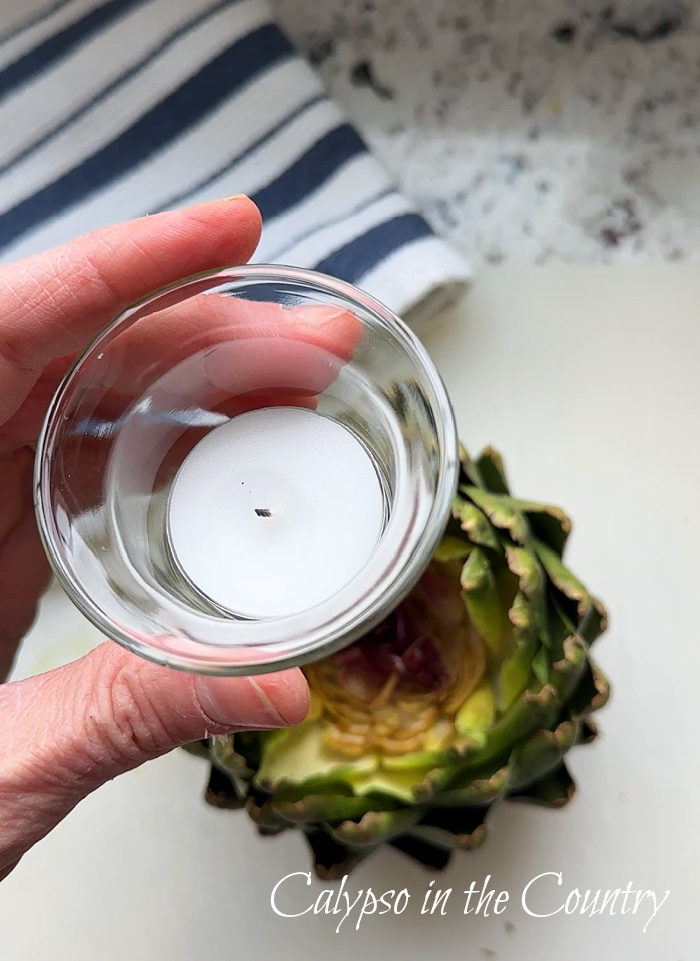 Hand holding a tealight over an artichoke
