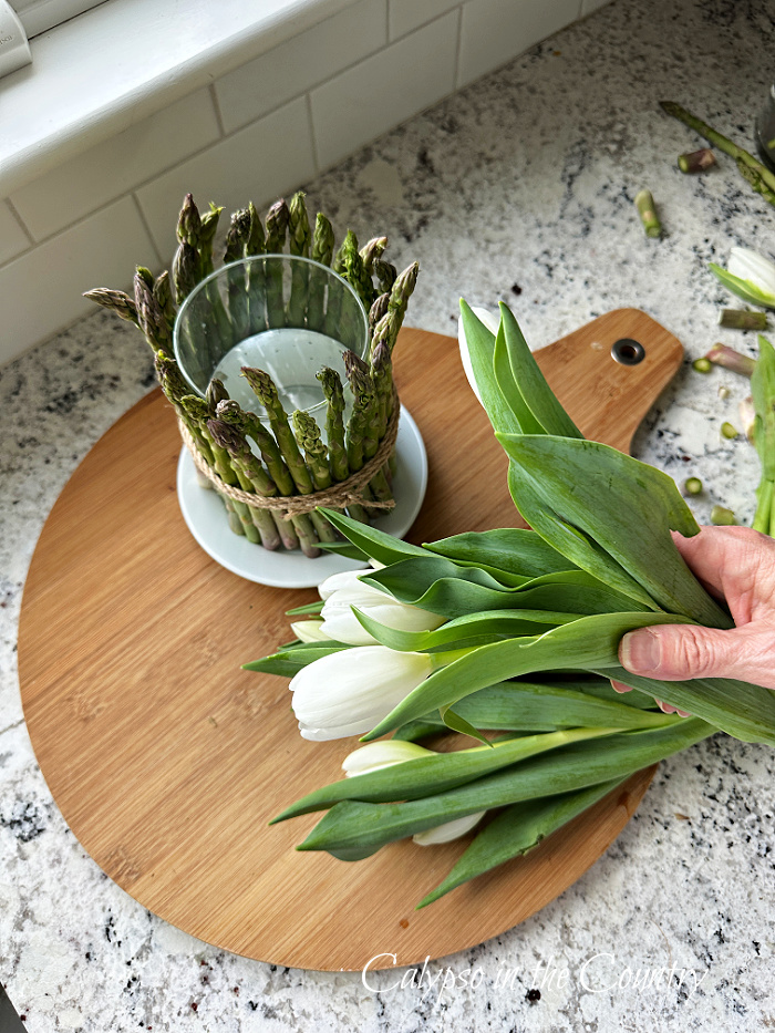Asparagus vase with white tulips on round cutting board