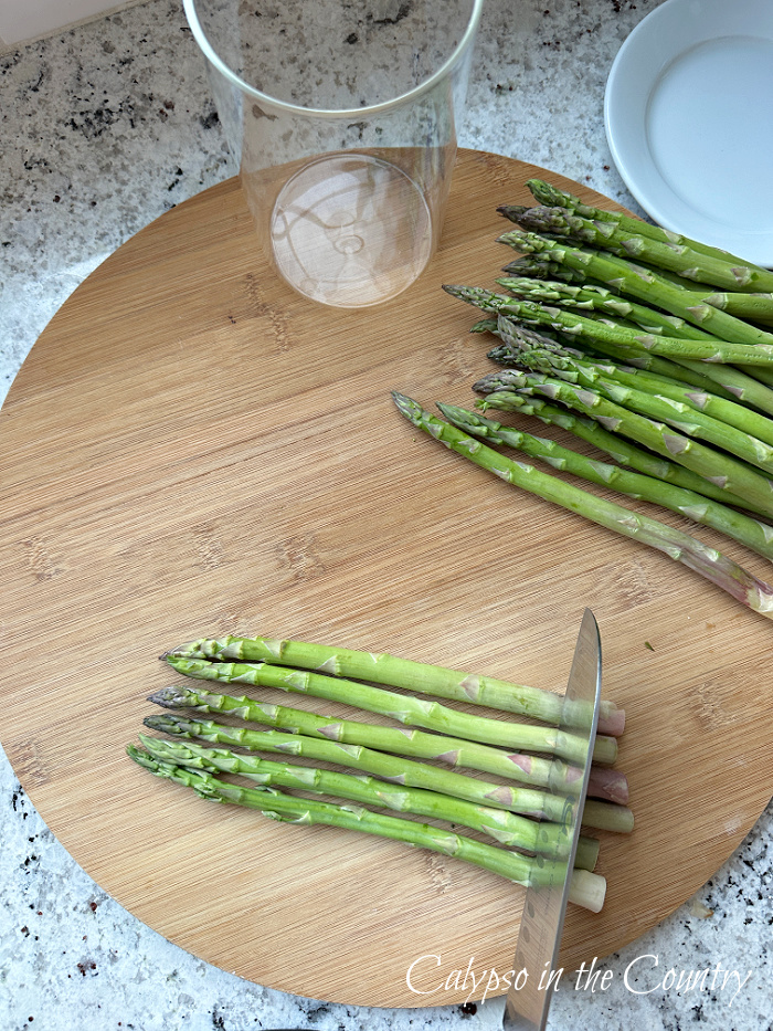 Round cutting board with asparagus stalks being sliced with a knife - asparagus vase tutorial