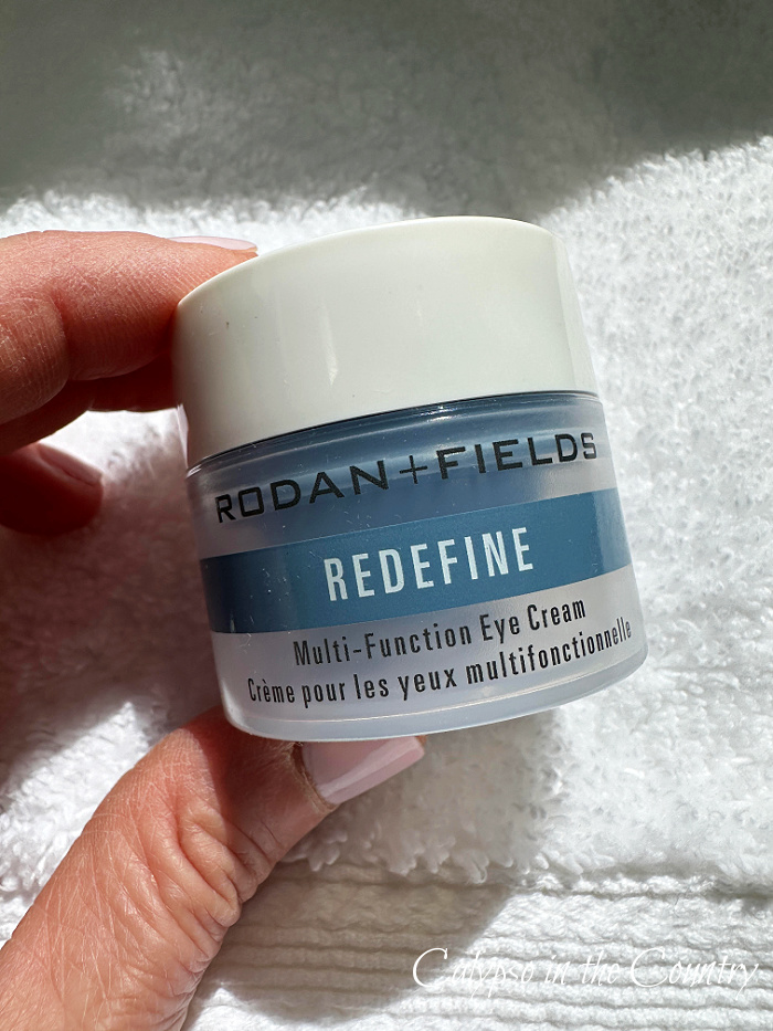 Hand holding blue and white jar of Rodan & Fields Redefine eye cream in front of white towel - March wrap up