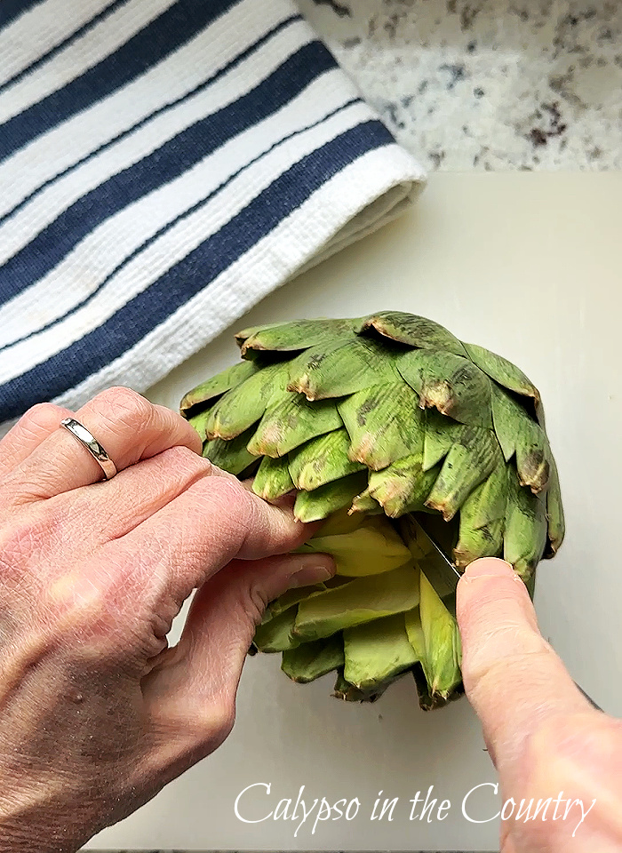 hands cutting inside of artichoke next to blue and white towel - artichoke candle holder diy