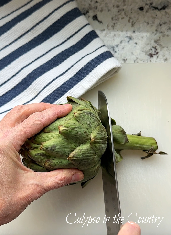 hand holding artichoke while cutting it with a knife - artichoke candle holder diy