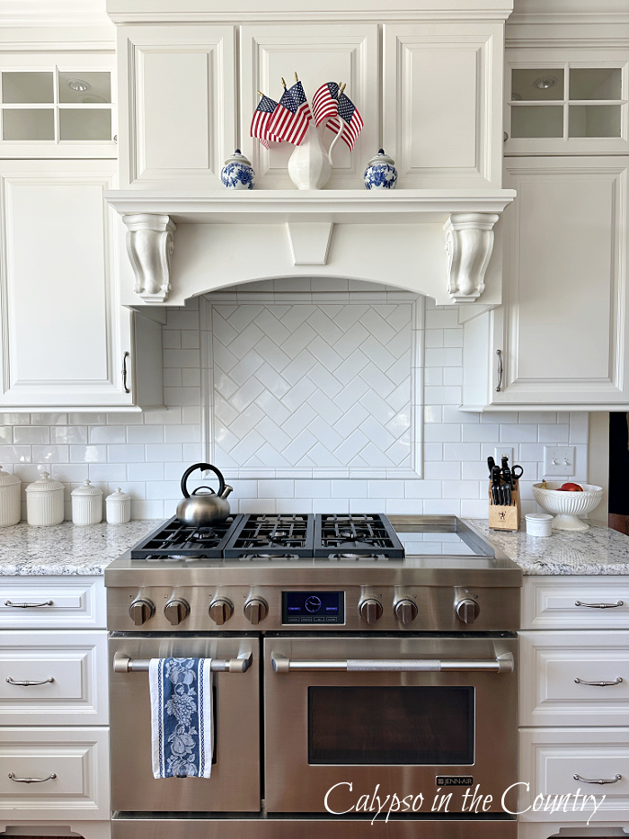 White pitcher of American flags on stove mantel in white kitchen - Decorating with American flags