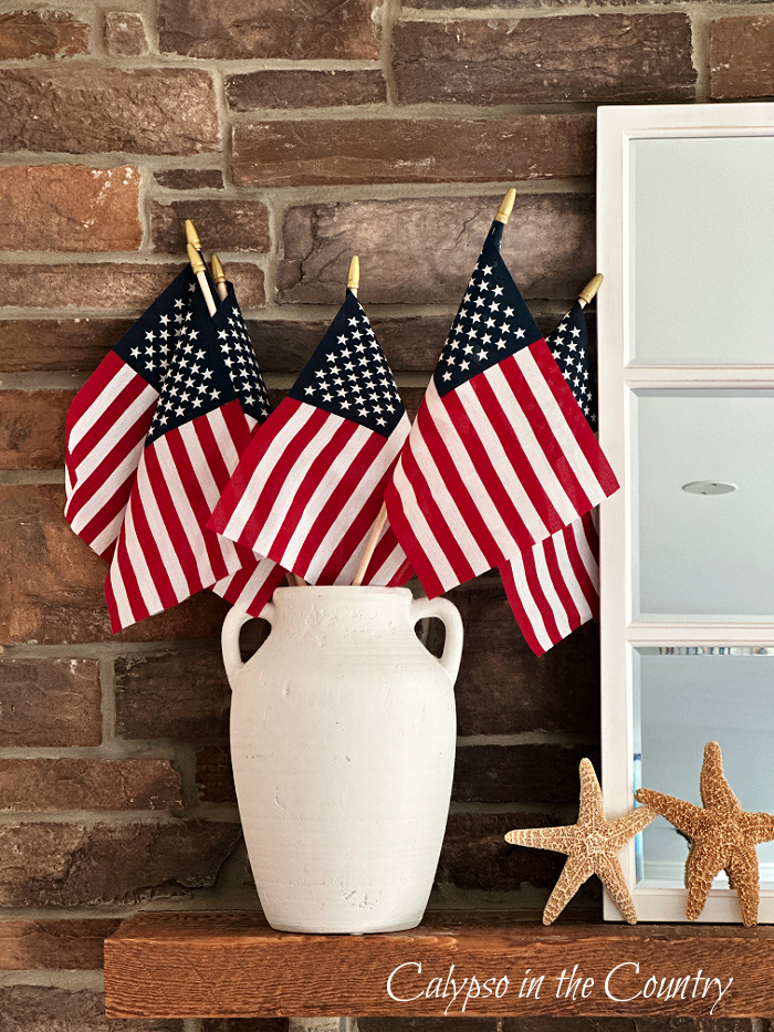 American flags in white vase wood mantel of stone fireplace - Decorating with American flags