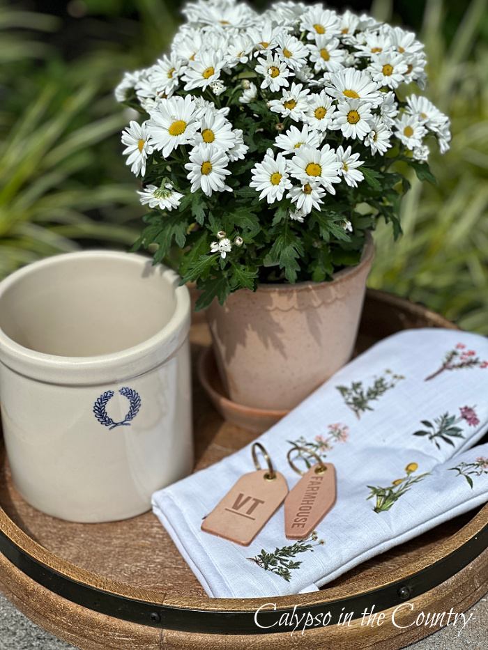 Potted flowers, ceramic crock, floral oven mitt and leather key chains on round tray - May wrap up