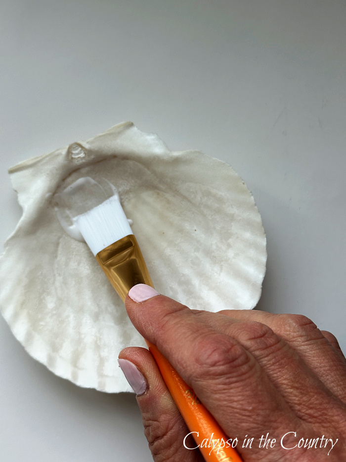Hand using paint brush on inside of shell - how to decoupage shells