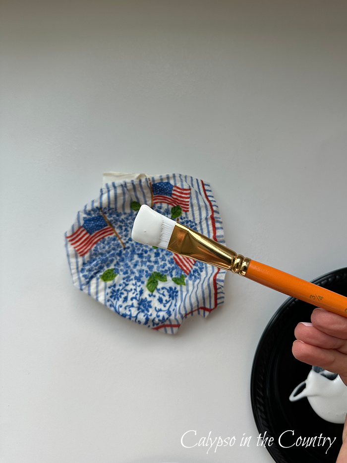 Paint brush applying Mod Podge to flag patterned shell
