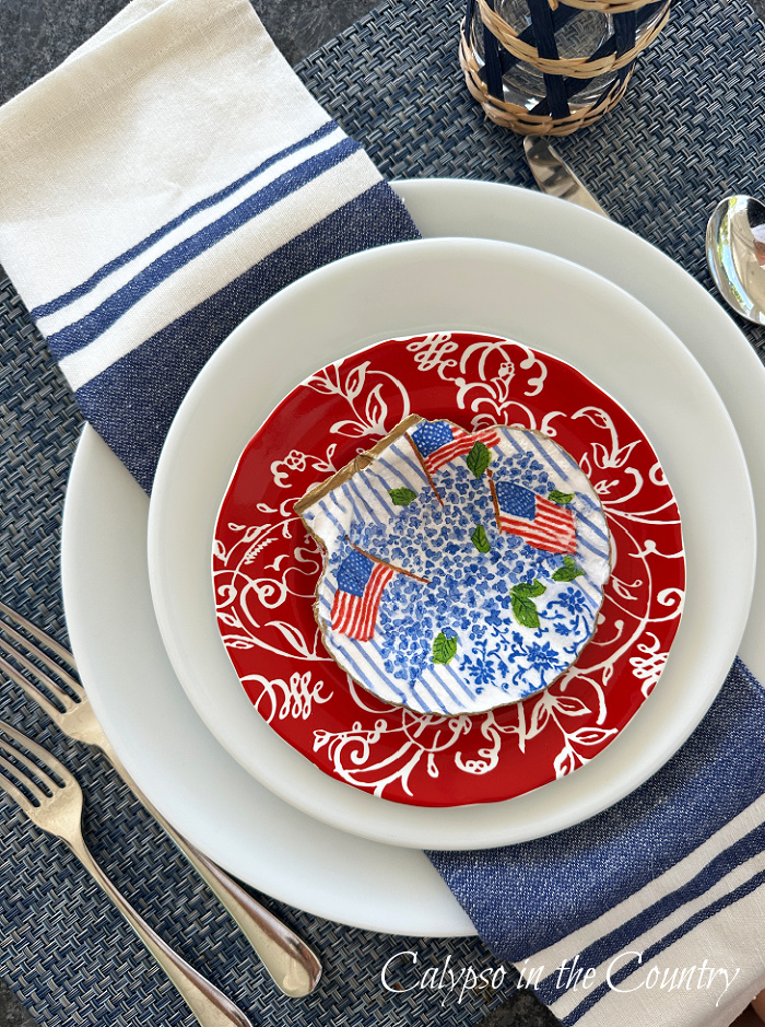 Flag patterned shell on top of stack of red and white plates with blue and white napkin - how to decoupage shells with napkins
