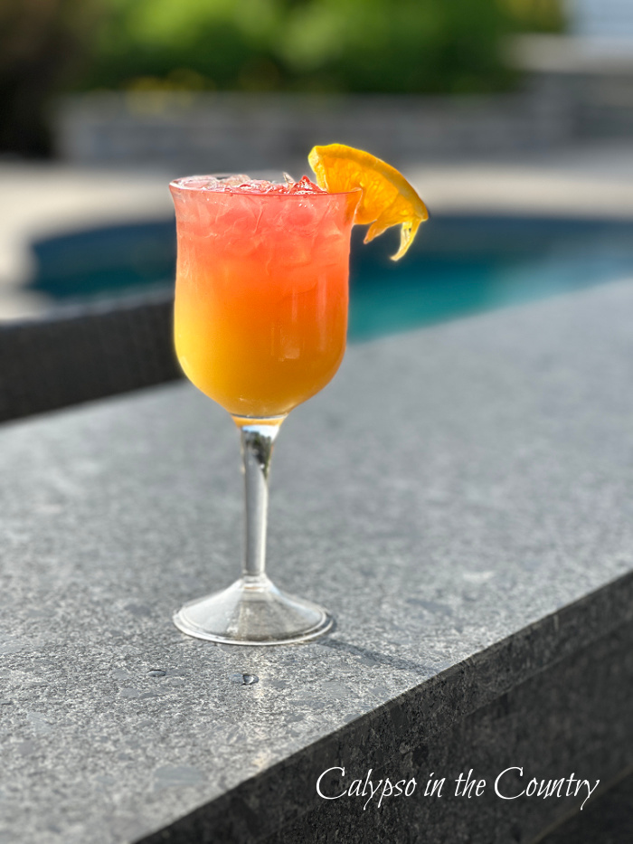 Tropical cocktail on gray counter with pool in background - June wrap up