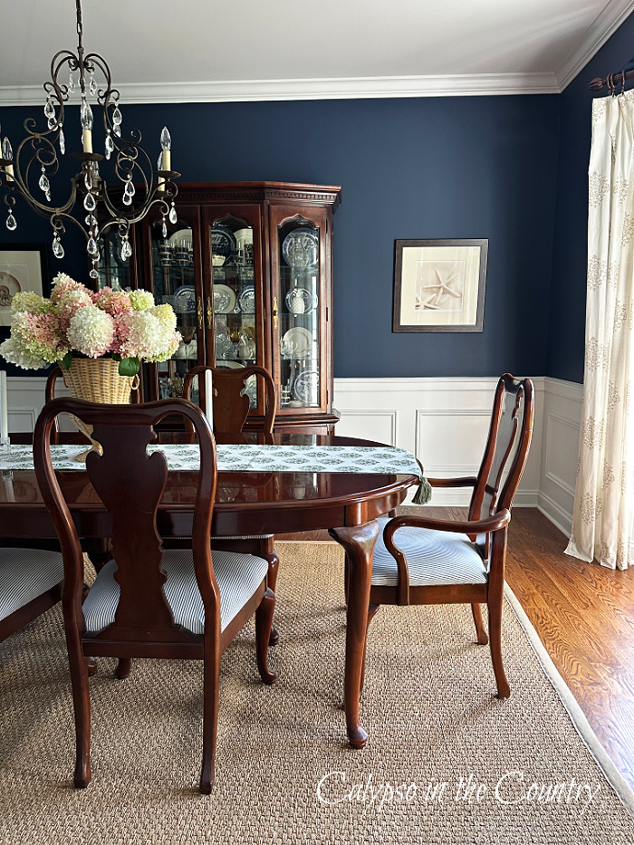 Pink and white hydrangeas in large woven vase on table in navy blue dining room - August home decor ideas