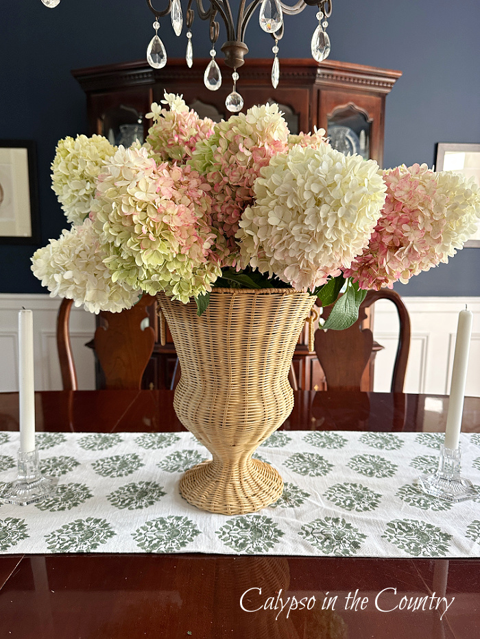 Pink and white hydrangeas in large woven vase on table in navy blue dining room - August home decor ideas