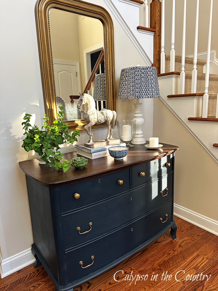 Blue dresser decorated with lamp, plant, candles and gold mirror above - August home decor ideas