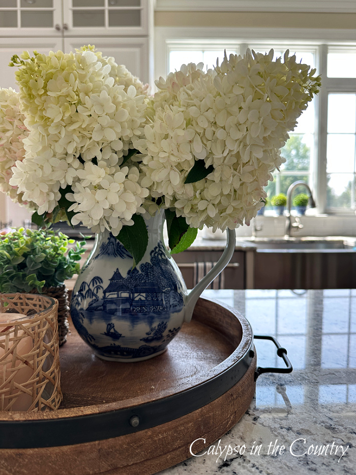 white hydrangeas in blue and white pitcher on round tray on kitchen counter - July wrap up