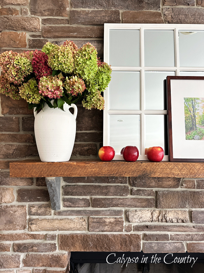 Fall mantel with white vase of hydrangeas, white window pane mirror and three red apples - decorating with apples