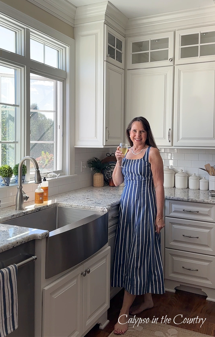 woman in blue dress holding a wine glass next to sink and window in a white kitchen - September wrap up