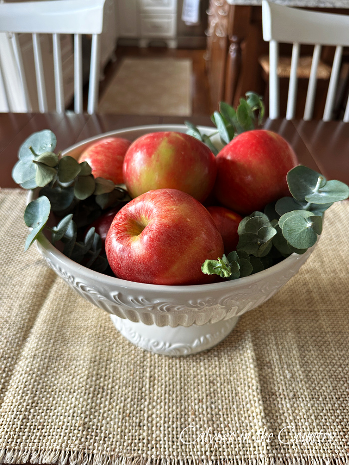 White bowl filled with apples and eucalyptus on dining table