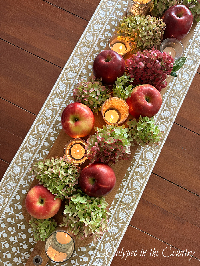 Apples, hydrangeas and candles on table runner