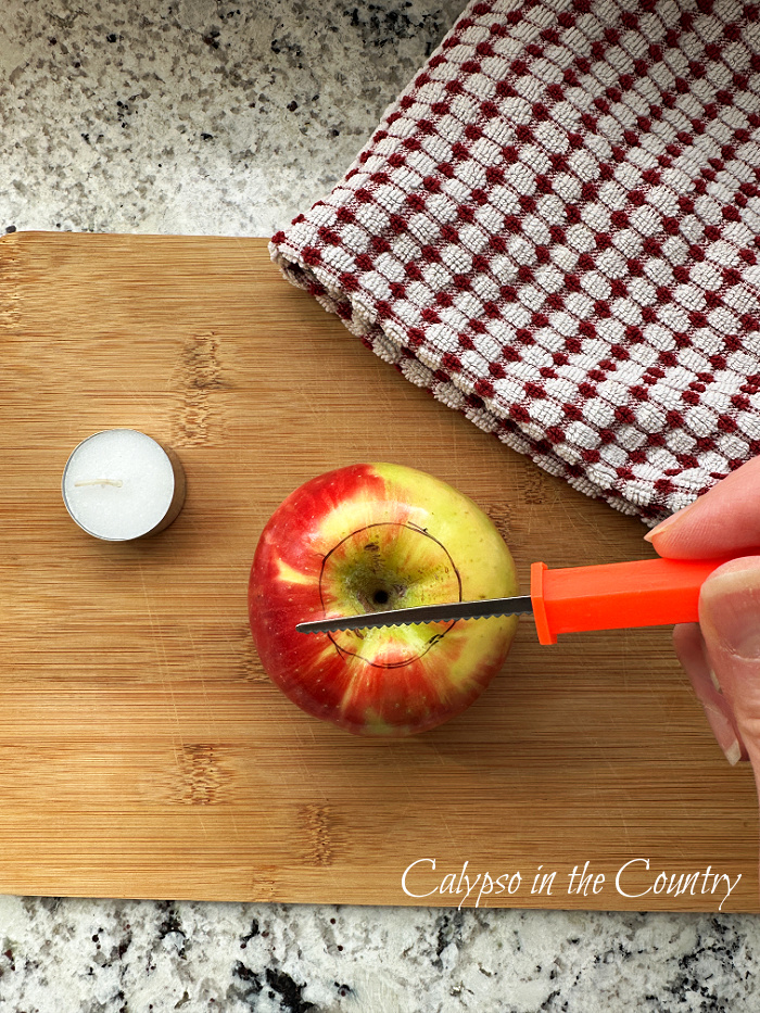 apple on cutting board with tea light and orange pumpkin carving tool - diy apple candle holders